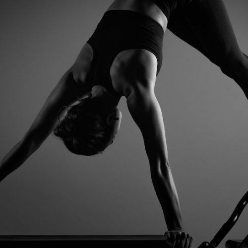 Young girl doing pilates exercises with a reformer bed. Beautiful slim fitness trainer on reformer gray background, low key, art light. Fitness concept
